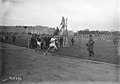 Photographie en noir et blanc d'une course à pied sur un stade en terre.