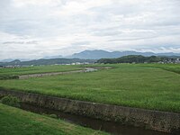 幸袋地域（現在は飯塚市の一部）の遠賀川。「この川のゆるやかな土堤は草に蔽われ、牛などが放牧してあって大そう牧歌的で、川すじなどという気分は感じられなかった。早春には、Hの妻と妹とがこの川の横で芹を摘み、つくしを採った」（「暗い活字」）。