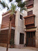 A front view of a large, white building standing behind a thin palm tree.