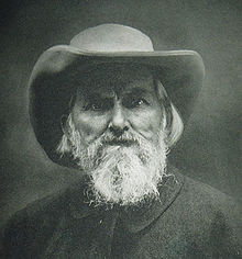 Portrait en noir et blanc d'un homme avec une barbe blanche et un chapeau aux bords larges.