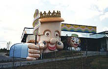 Photographie d'un bâtiment avec, sur la façade, le visage d'un personnage géant et sa main tenant une friandise.