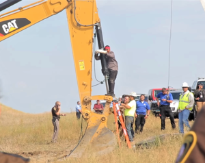 Color image of Lakota man locked down to construction equipment at direct action against Dakota Access Pipeline