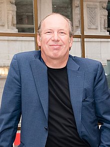 Porträt von Hans Zimmer. Er trägt einen blauen Anzug und hat einen gemächlichen Körperausdruck.