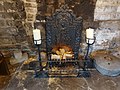 A close-up view of Ilkley Manor House's fireplace in the main hall. On the top right, you can just about see a rectangle where there was possibly a bread oven. There is a black metal fireback which is possibly Victorian or Edwardian. The fire itself is a replica using electrical lights to create a flame effect and real logs. There are also two battery-operated candles in holders on either side of the fire.