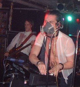A singer, Mike Patton, performing in an elastomeric respirator (but without its filter cartridges) in 2002. Note microphone.