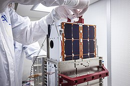 A person in a labcoat handles a box-sized satellite bus.