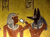 «Anubis gir livsånde til Thutmosis IV», freske i gravkammeret KV 43 i Kongenes dal fra det 18. egyptiske dynasti. Anubis, guddom for dødsriket og balsamering, ble framstilt som sjakal, gjerne med hankekorset (ankh) som livssymbol.