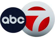 A white 7 in a white circle with red filled in. The ABC network logo, a black disk with lowercase letters a b c, overlaps it on the left side.