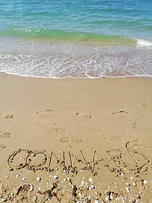 Le mot connard, dérivé de con, écrit sur le sable.