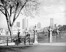 Photographie en noir et blanc d'un portail donnant sur un parc avec une vue sur le centre-ville de Montréal.