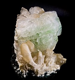 Fluorapofilita-(K) (alto) com estilbita (base). Pedreira Nasik, distrito de Nashik, Maarastra, Índia. Tamanho: 10,3 × 7,2 cm. A fluoropofilita-(K) é um mineral relativamente frequente, como produto da atividade hidrotermal de baixa temperatura, nas cavidades de rochas vulcânicas e de granitos, também ocasionalmente em veios metalíferos. Está associada à estilbita e outros zeólitos, bem como calcita e quartzo. (definição 1 818 × 1 818)