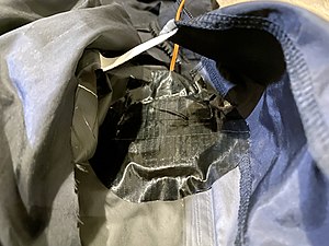 The inner taffeta lining cut open, exposing the outermost fabric from the inside which is then scored with a blade. The squib device is then aligned to the hole and attached with duct tape.