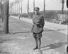 Photo en noir et blanc d'un militaire de la première guerre mondiale qui se tient au bord d'une route.