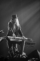 Photo en noir et blanc d'un homme avec un chapeau jouant du clavier sur une scène.