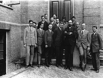 Fifteen men in suits, and one womyn, pose for a group photograph