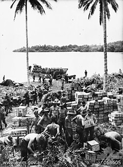 Crates of stores being unloaded from landing craft by soldiers and stacked on the shore