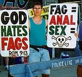 Le militant de la Westboro Baptist Church Benjamin Phelps arborant des pancartes homophobes proclamant « Dieu hait les pédés » et « Pédés = sexe anal = mort » (2005).