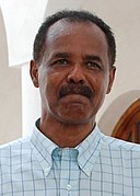 Photographie du représentant du Gouvernement érythréen dans la ville de Massaoua, un homme de couleur de peau noire, à la moustache et aux cheveux noirs, portant une chemise bleu claire à carreaux bleus foncés.