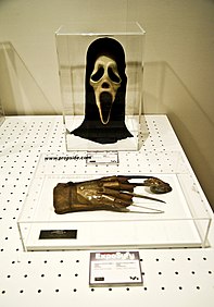 Photo d'un masque blanc et d'un gant avec des lames, enfermés dans boites en verre.