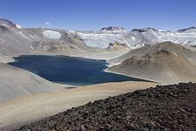 A blue lake in a crater, with the terrain covered in rocks and no vegetation