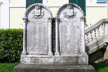 A color photo of two stone memorials, each with approximately 6 feet tall. The WW2 memorial stands on the left, with 46 names inscribed, and the WWI memorial adjoins it on the right, with 42 names inscribed.