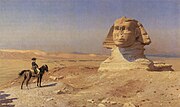 Person on a horse looks towards a giant statue of a head in the desert, with a blue sky