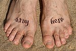 Ambigram tattoo Stay here written on feet