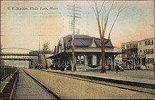 A postcard of a wooden railway station with a mansard roof