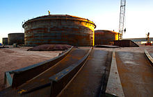 Plusieurs grands réservoirs cylindriques de couleur brune et grise foncée en construction.