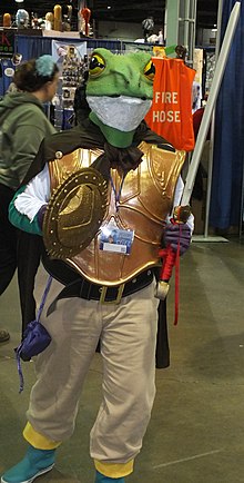 Homme équipée d'un bouclier et d'une épée, et portant un masque de grenouille.