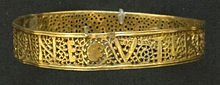 A gold bracelet with a pattern and writing created by making holes in the bracelet