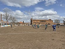 Campo Municipal de Futbol de la Azucarera, con las antiguas escuelas y la chimenea dela Azucarera del Jiloca al fondo