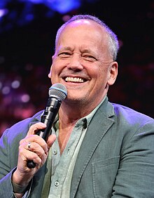 smiling dark-haired man with glasses at microphone