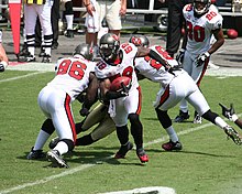 A man in a white American football uniform runs with a football on a football field