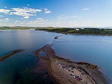 aerial view of line of cars waiting for tide to recede to drive to Ministers Island; sandbar visible, though still partially covered with water.