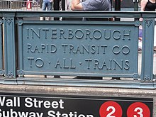 Detail eines Bahnhofseingang: Ein Blechschild als Teil der Brüstung, mit der dreizeiligen Inschrift „Interborough / Rapid Transit Co / To All Trains“