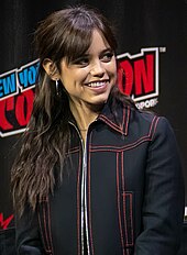 Ortega, wearing a black jacket, smiling towards her left