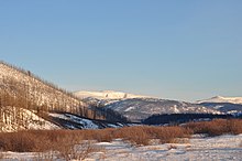 Fotografía dunha paisaxe no inverno, coas árbores espidas, e os vales e montañas cubertos de neve