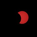Photography of a partial solar eclipse, with the sun's orange disk being partially occulted by the moon on a black background.