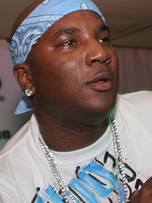 A black man with a blue bandana and a chain, lightly smiling at an off-screen entity