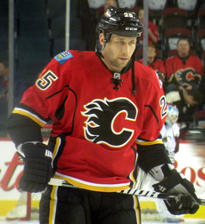 Upper body of a man staring intently into the distance. He is in a full hockey uniform; the jersey is red with black and yellow trim, and a black stylized "C" logo on his chest.