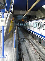 Stasiun bawah tanah dengan dua jalur di Madrid. Kereta bawah tanah biru dan putih memasuki stasiun di sebelah kiri.