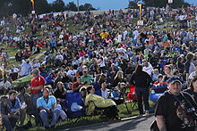 A crowd of people sitting on grass and in folding chairs