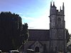 Gray stone building with prominent four stage tower at the right hand end. To the left is a large yew tree.