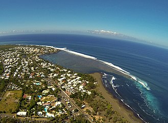 Une plage de sable noir, où une pointe de récif fait naître d'importantes vagues, propices au surf.