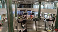 Open view of the wide concourse level with pillars supporting the structure. A set of escalators ahead leads to the underground platforms.