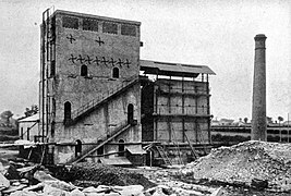 Photo en noir et blanc montrant un haut bâtiment en pierre et une cheminée d'usine.