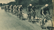 Photo en noir et blanc d'un peloton cycliste sur une route de campagne.