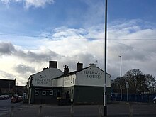 Photo of the Halfway House pub, Stanningley Leeds, showing the painted inn name on the end and side of the pub, with a cloudy and blue sky above