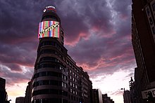 The corner of a building with neon signs advertising Capitol, Vodafone and Schweppes.